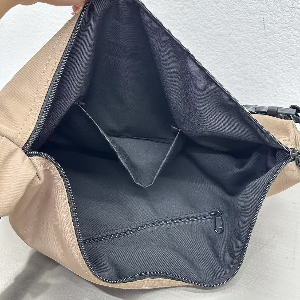 Close-up of a beige bag with a black interior pocket on a light gray background,Convertible nylon tote bag with detachable crossbody strap, zippered front pocket, and main compartment. Available in olive green, black, and beige.