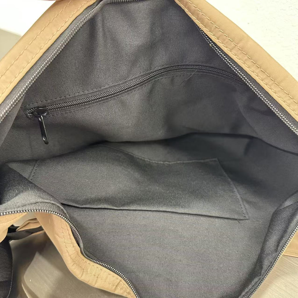 Open beige bag with black interior lining on a light wooden surface,Convertible nylon tote bag with detachable crossbody strap, zippered front pocket, and main compartment. Available in olive green, black, and beige.