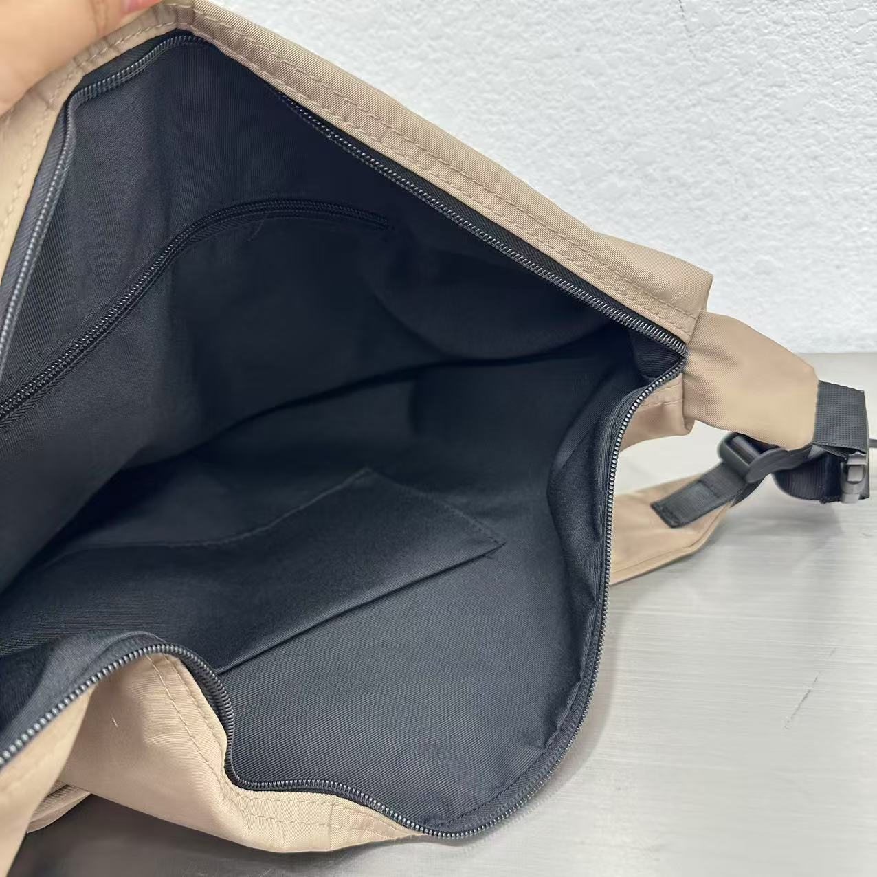 Open beige bag with black interior on a light gray background,Convertible nylon tote bag with detachable crossbody strap, zippered front pocket, and main compartment. Available in olive green, black, and beige.