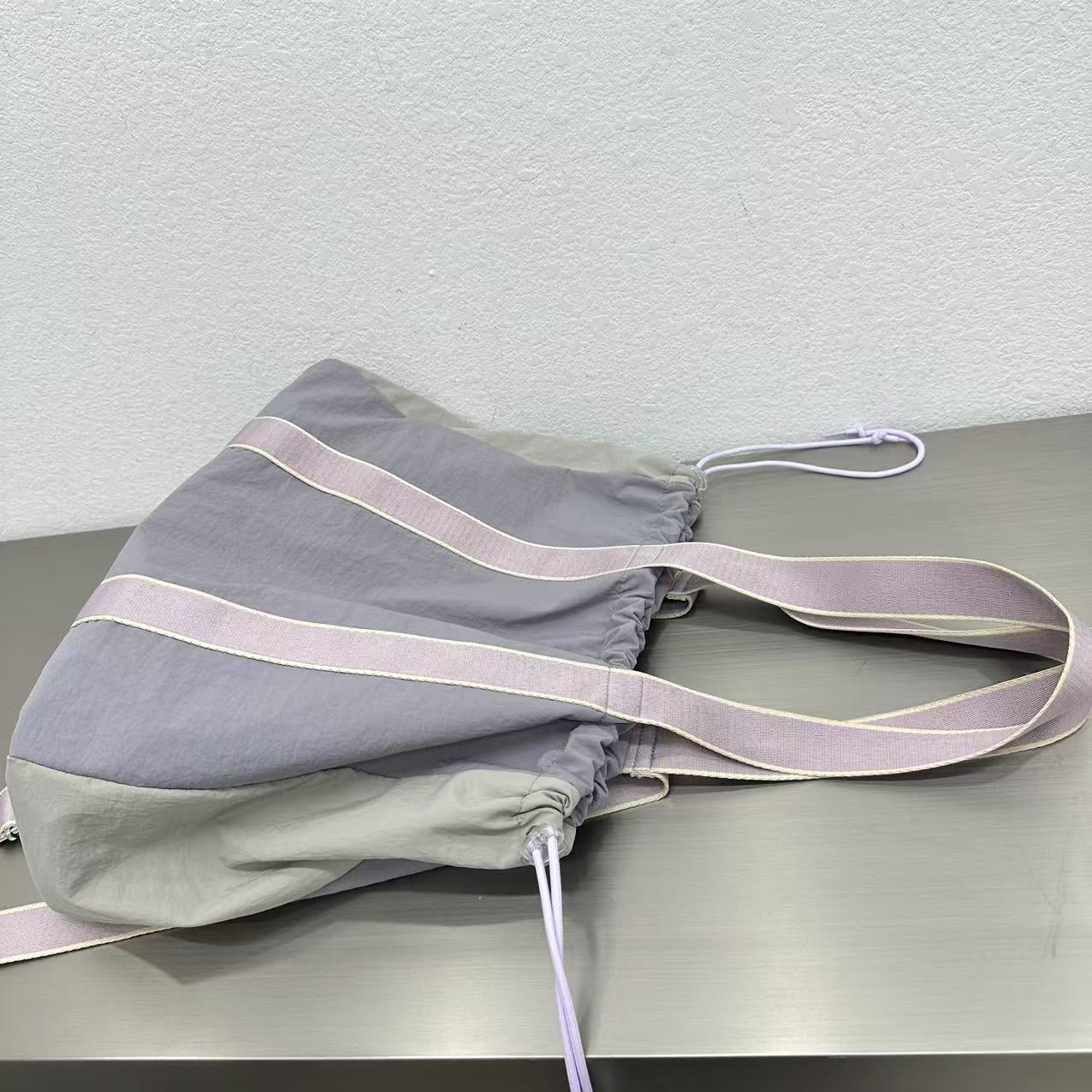 Gray drawstring bag with a strap on a light gray surfaceA versatile and stylish tote bag for women, perfect for the Indian market, shot from a side angle showing the product in use. The bag is made from a durable, high-quality fabric and features a casual, comfortable design with shoulder straps. This fashion accessory is ideal for a daily commute, college, or casual outings. It's a must-have for those seeking a practical yet trendy handbag in India.