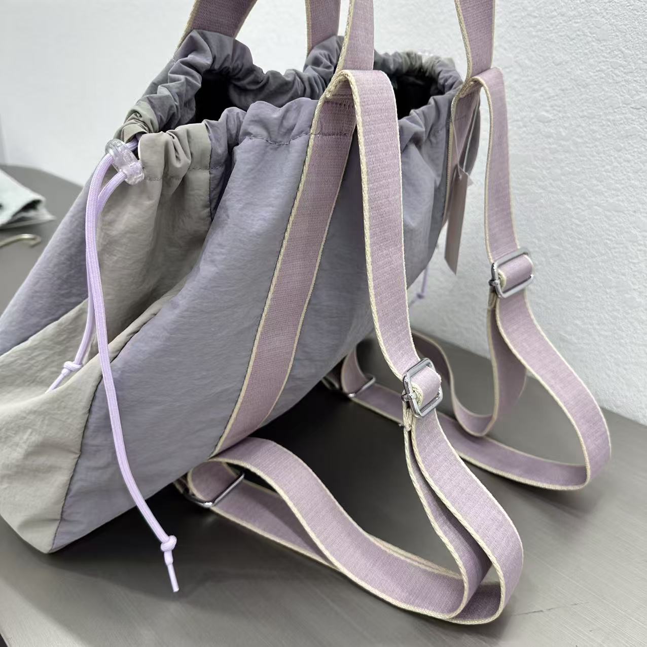 Gray bag with purple straps on a light gray surface.A versatile and stylish tote bag for women, perfect for the Indian market, shot from a side angle showing the product in use. The bag is made from a durable, high-quality fabric and features a casual, comfortable design with shoulder straps. This fashion accessory is ideal for a daily commute, college, or casual outings. It's a must-have for those seeking a practical yet trendy handbag in India.