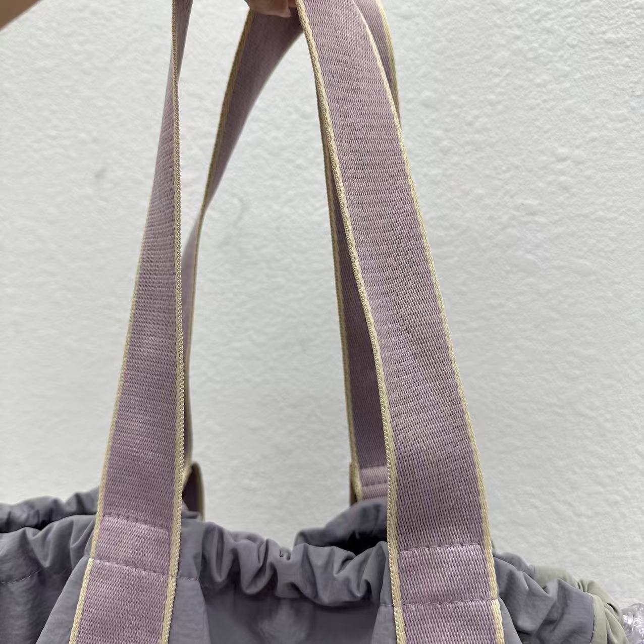 Close-up of a gray bag with purple straps on a light gray background,A versatile and stylish tote bag for women, perfect for the Indian market, shot from a side angle showing the product in use. The bag is made from a durable, high-quality fabric and features a casual, comfortable design with shoulder straps. This fashion accessory is ideal for a daily commute, college, or casual outings. It's a must-have for those seeking a practical yet trendy handbag in India.