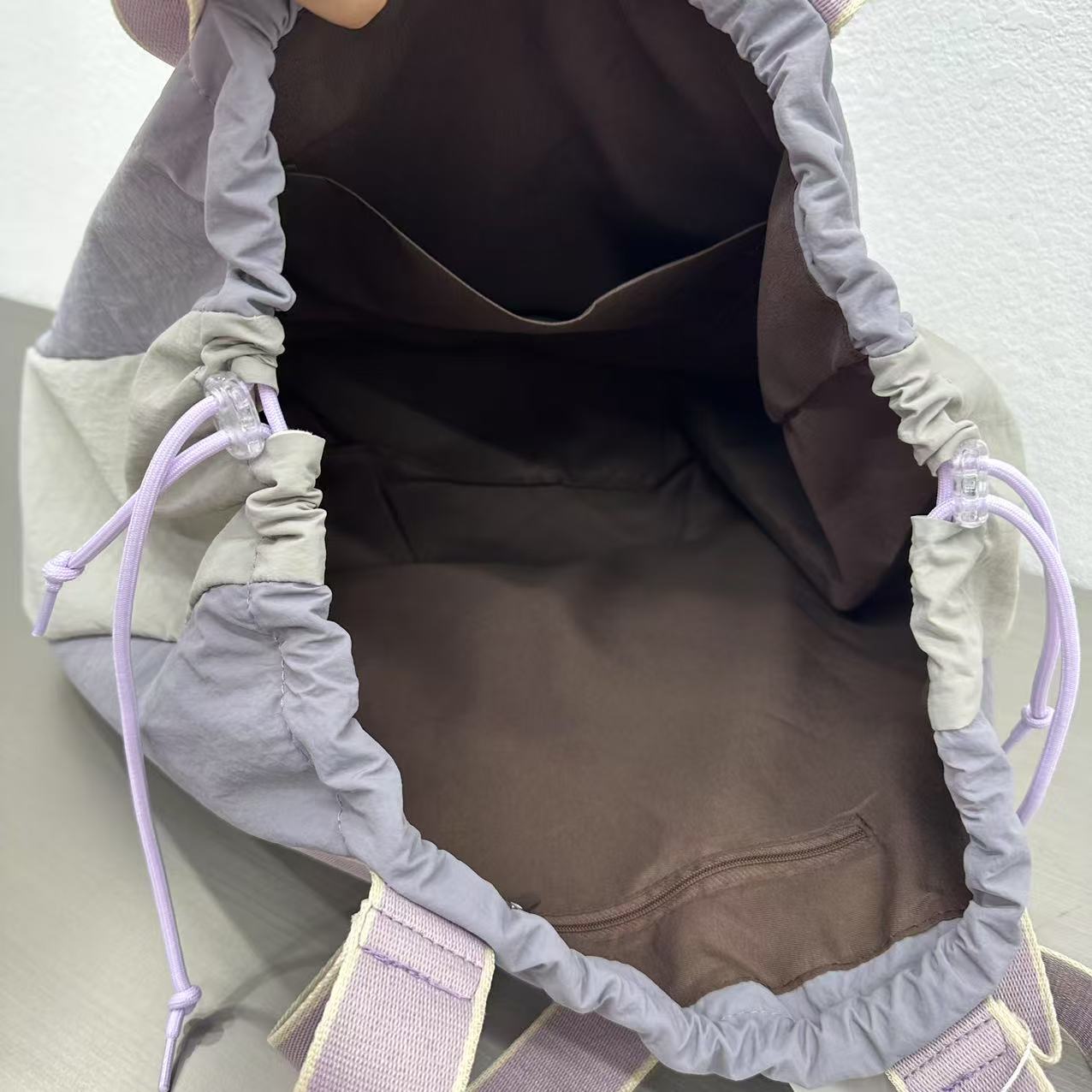 Close-up of a brown bag with gray drawstrings and purple accents on a light gray background,A versatile and stylish tote bag for women, perfect for the Indian market, shot from a side angle showing the product in use. The bag is made from a durable, high-quality fabric and features a casual, comfortable design with shoulder straps. This fashion accessory is ideal for a daily commute, college, or casual outings. It's a must-have for those seeking a practical yet trendy handbag in India.