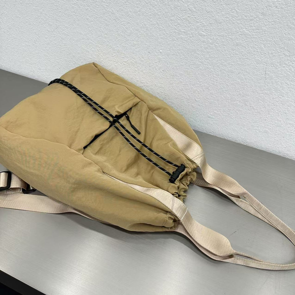 Beige bag with black straps on a gray surface."Stylish khaki drawstring tote bag with multiple compartments and adjustable straps, perfect for daily use, shopping, and travel in India. Features include a secure zippered pocket, spacious main compartment, and comfortable shoulder straps. Ideal for fashion-conscious individuals seeking a versatile and trendy bag."