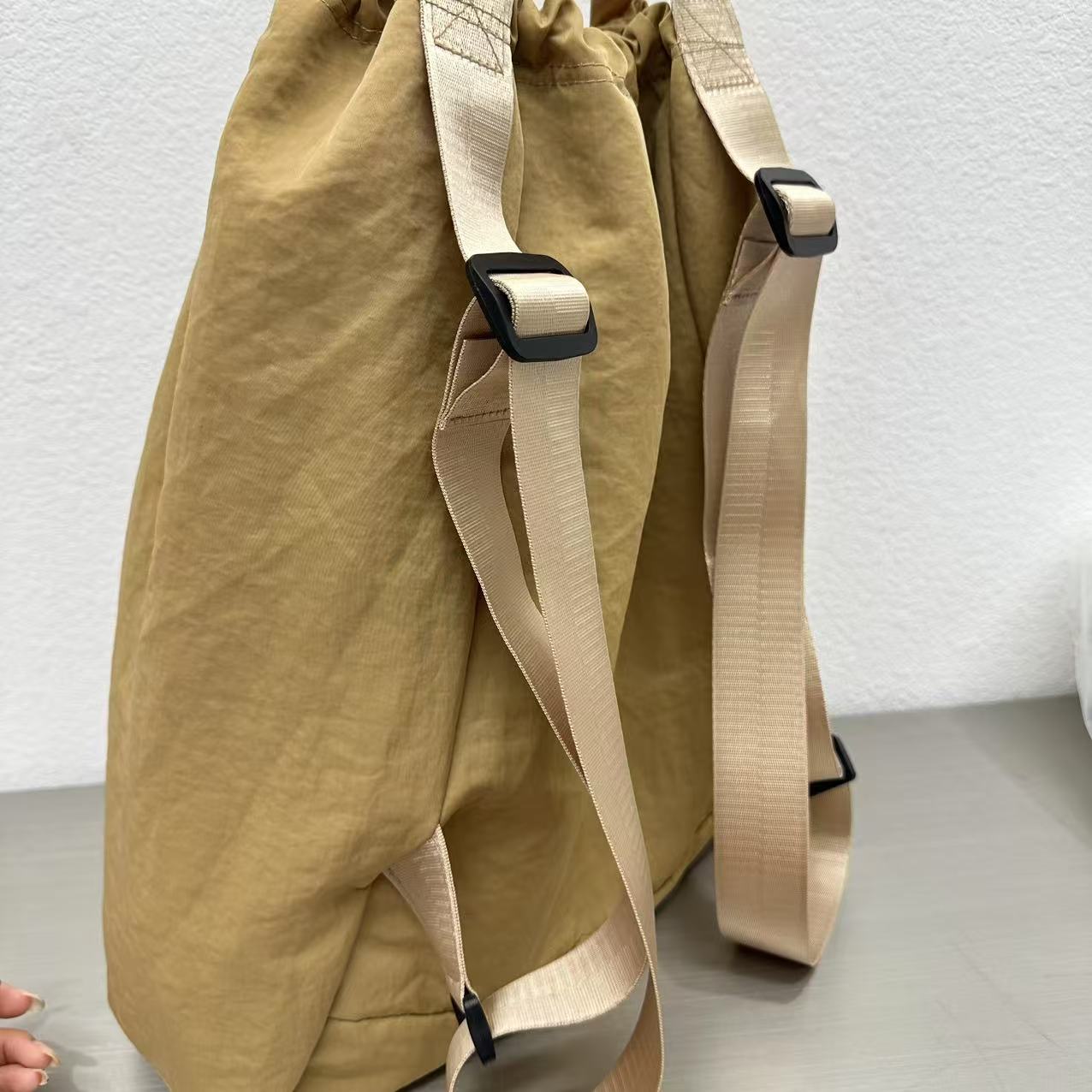 Beige backpack with straps on a light gray surface,"Stylish khaki drawstring tote bag with multiple compartments and adjustable straps, perfect for daily use, shopping, and travel in India. Features include a secure zippered pocket, spacious main compartment, and comfortable shoulder straps. Ideal for fashion-conscious individuals seeking a versatile and trendy bag."