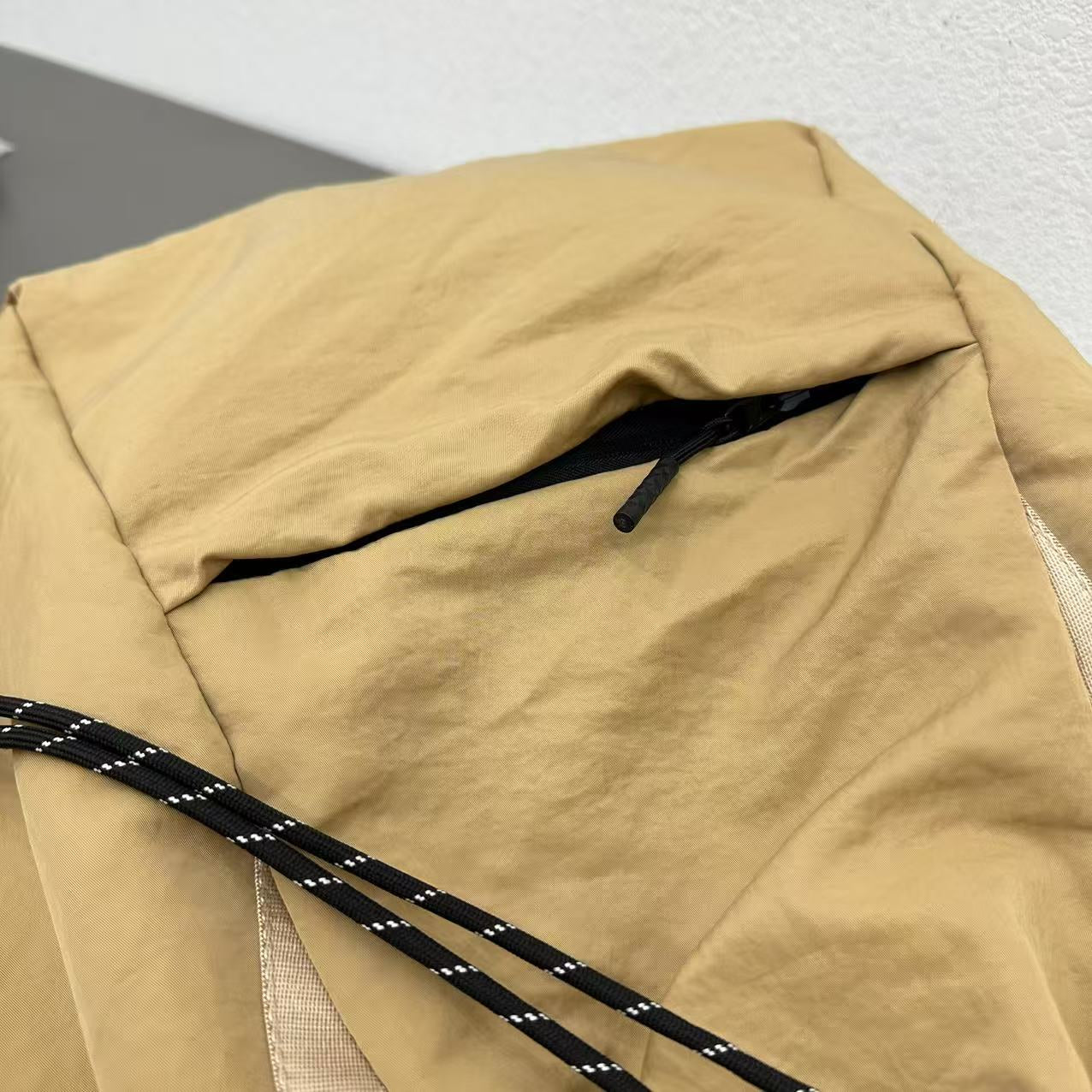 Close-up of a beige backpack with black drawstrings on a light gray background,"Stylish khaki drawstring tote bag with multiple compartments and adjustable straps, perfect for daily use, shopping, and travel in India. Features include a secure zippered pocket, spacious main compartment, and comfortable shoulder straps. Ideal for fashion-conscious individuals seeking a versatile and trendy bag."