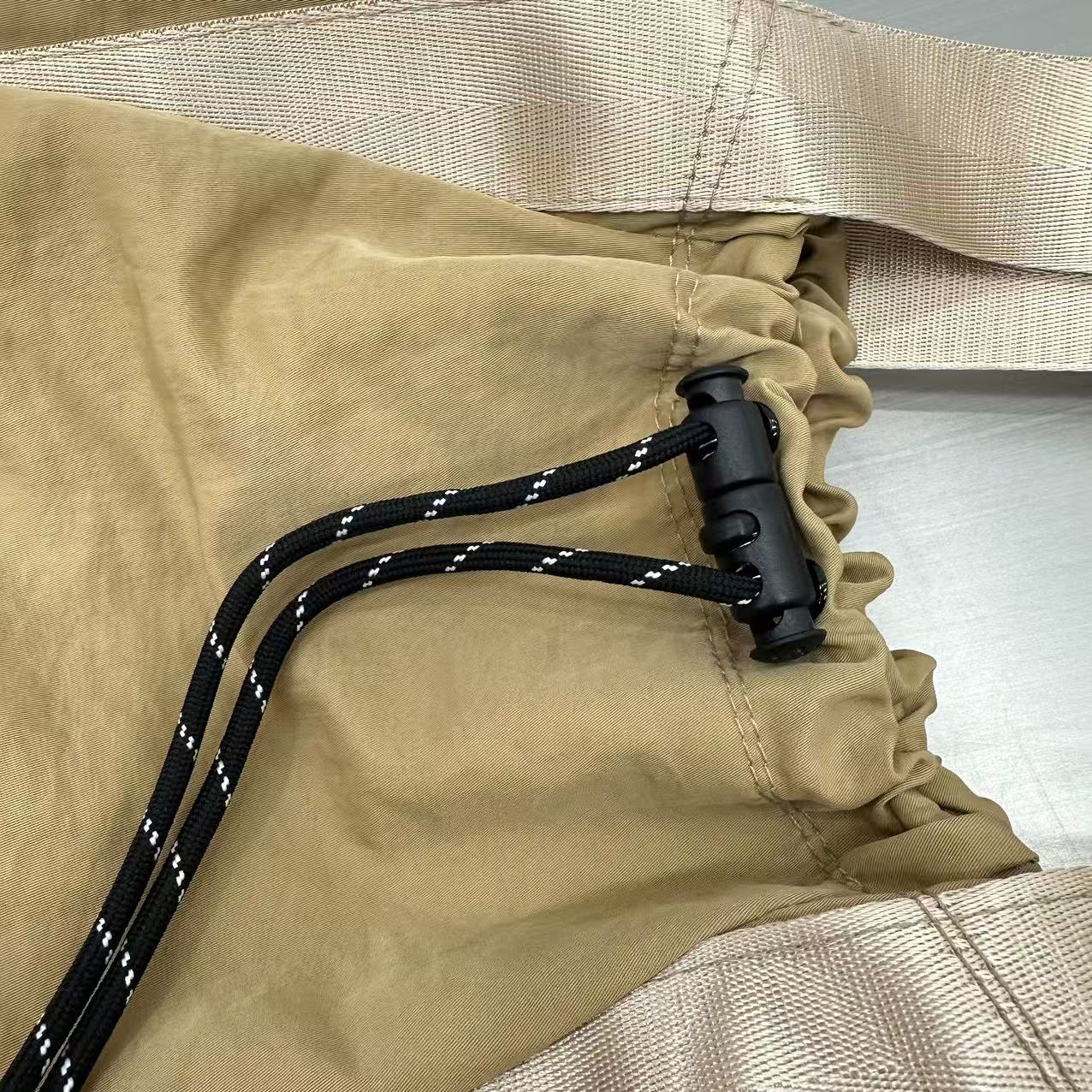 Close-up of beige fabric with a black cord and buckle,"Stylish khaki drawstring tote bag with multiple compartments and adjustable straps, perfect for daily use, shopping, and travel in India. Features include a secure zippered pocket, spacious main compartment, and comfortable shoulder straps. Ideal for fashion-conscious individuals seeking a versatile and trendy bag."