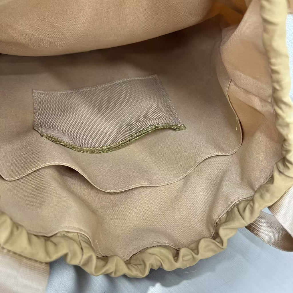 Close-up of a beige fabric with a mesh pocket on a light blue background,"Stylish khaki drawstring tote bag with multiple compartments and adjustable straps, perfect for daily use, shopping, and travel in India. Features include a secure zippered pocket, spacious main compartment, and comfortable shoulder straps. Ideal for fashion-conscious individuals seeking a versatile and trendy bag."