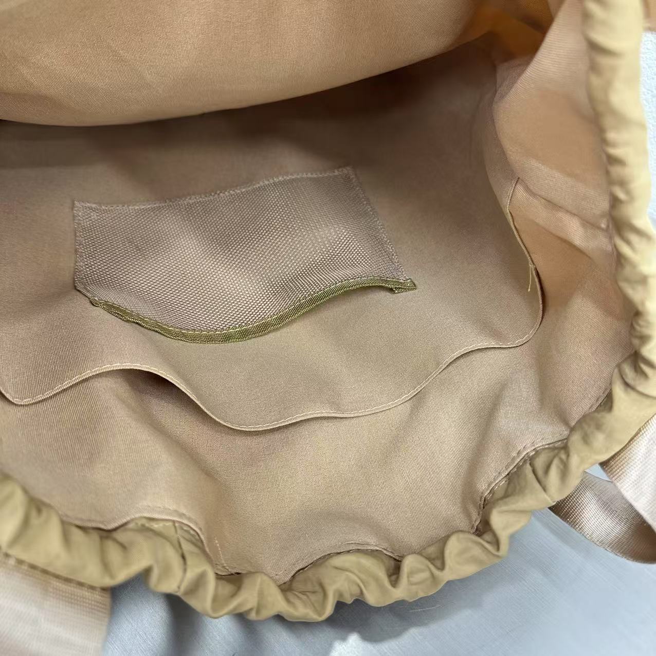 Close-up of a beige fabric with a mesh pocket on a light blue background,"Stylish khaki drawstring tote bag with multiple compartments and adjustable straps, perfect for daily use, shopping, and travel in India. Features include a secure zippered pocket, spacious main compartment, and comfortable shoulder straps. Ideal for fashion-conscious individuals seeking a versatile and trendy bag."