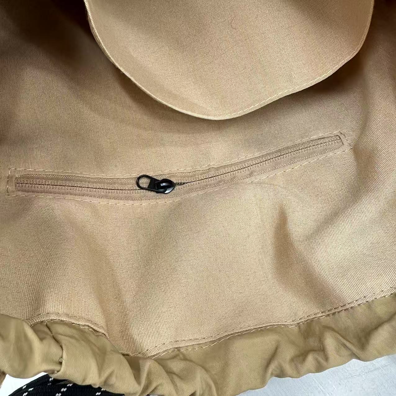 Close-up of a beige fabric with a zipper, likely part of a garment,"Stylish khaki drawstring tote bag with multiple compartments and adjustable straps, perfect for daily use, shopping, and travel in India. Features include a secure zippered pocket, spacious main compartment, and comfortable shoulder straps. Ideal for fashion-conscious individuals seeking a versatile and trendy bag."