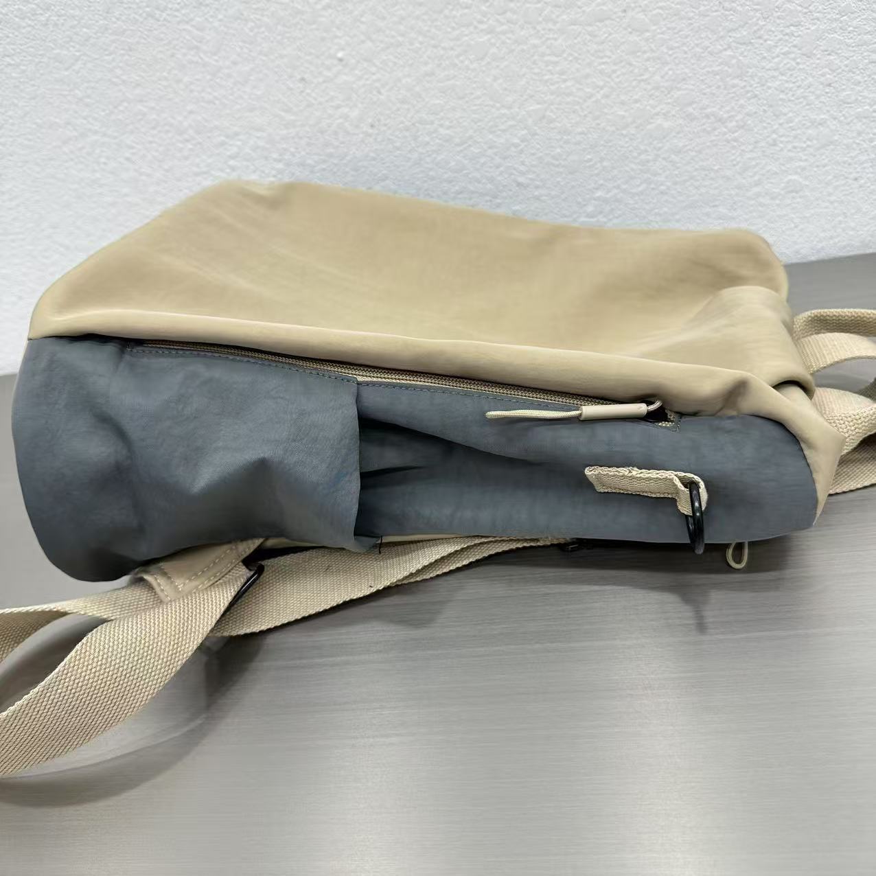 Folded beige and gray fabric bag on a metallic surface with a light grayStylish travel backpack, durable everyday bag, versatile shoulder tote, convertible backpack purse, waterproof utility bag, modern casual rucksack, ergonomic daypack, trendy laptop bag, multi-functional women's backpack, secure anti-theft design, spacious college bag, fashion-forward accessory, urban commuter pack, comfortable carry-all, premium quality satchel, practical work bag, chic student backpack, easy-access travel es background
