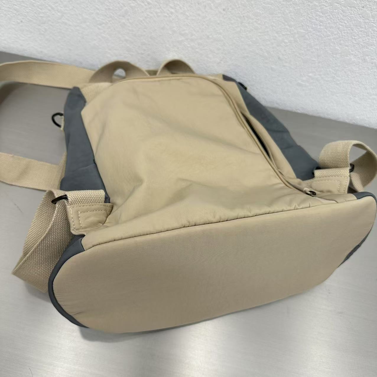 Beige backpack with gray accents on a metallic surfaceStylish travel backpack, durable everyday bag, versatile shoulder tote, convertible backpack purse, waterproof utility bag, modern casual rucksack, ergonomic daypack, trendy laptop bag, multi-functional women's backpack, secure anti-theft design, spacious college bag, fashion-forward accessory, urban commuter pack, comfortable carry-all, premium quality satchel, practical work bag, chic student backpack, easy-access travel essential, organized personal i