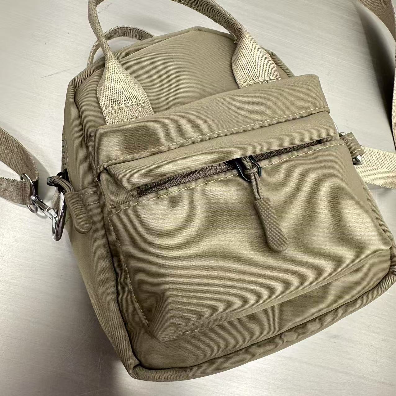 Beige backpack with a strap on a light gray background,A high-fashion shot of a woman in a black skirt and white shirt, holding a stylish, minimalist brown bag. The image is professionally lit in a studio against a clean white background, with a strong focus on the bag's sleek design and texture. The photo emphasizes a sophisticated and modern aesthetic, perfect for luxury or premium lifestyle brands.