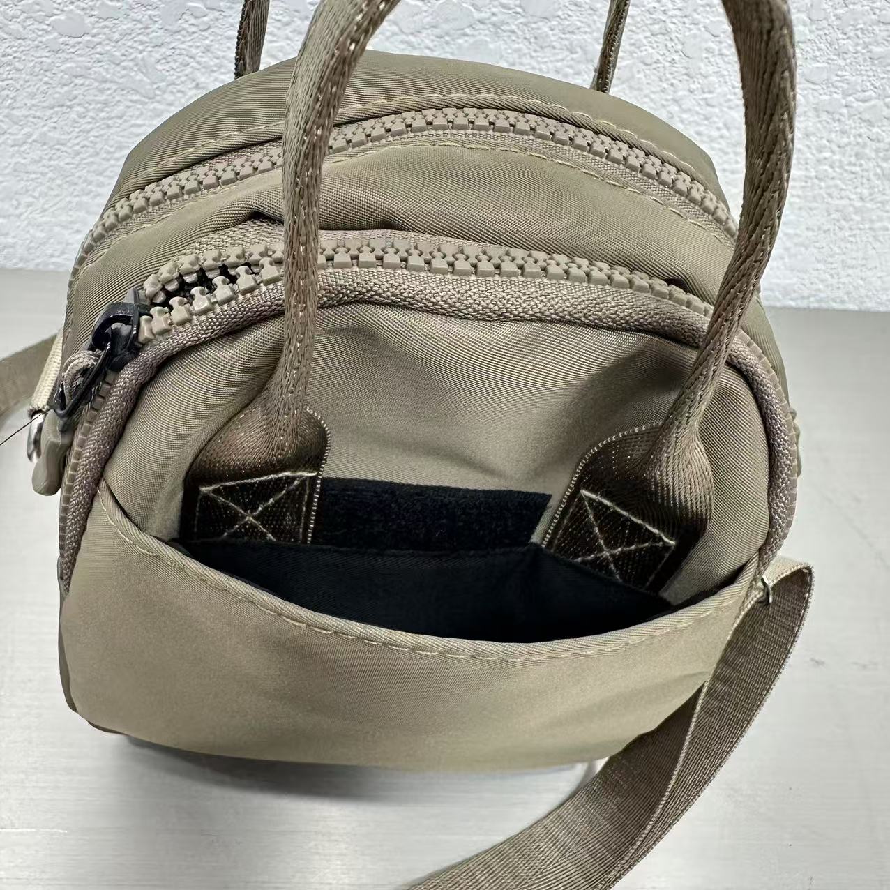 Beige bag with multiple zippers on a light gray background,A high-fashion shot of a woman in a black skirt and white shirt, holding a stylish, minimalist brown bag. The image is professionally lit in a studio against a clean white background, with a strong focus on the bag's sleek design and texture. The photo emphasizes a sophisticated and modern aesthetic, perfect for luxury or premium lifestyle brands.