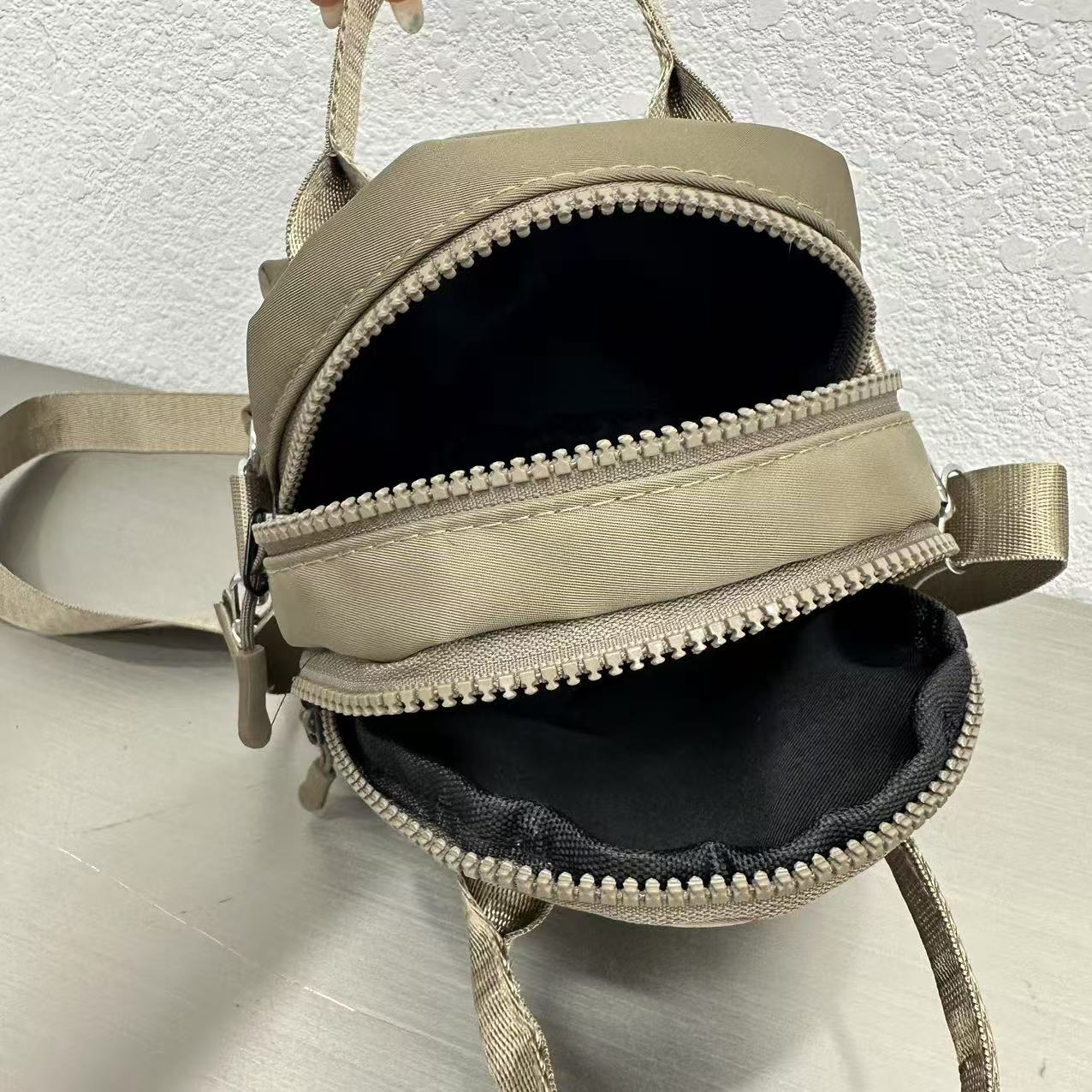 Small beige backpack with a zipper on a light gray backgroundA high-fashion shot of a woman in a black skirt and white shirt, holding a stylish, minimalist brown bag. The image is professionally lit in a studio against a clean white background, with a strong focus on the bag's sleek design and texture. The photo emphasizes a sophisticated and modern aesthetic, perfect for luxury or premium lifestyle brands.