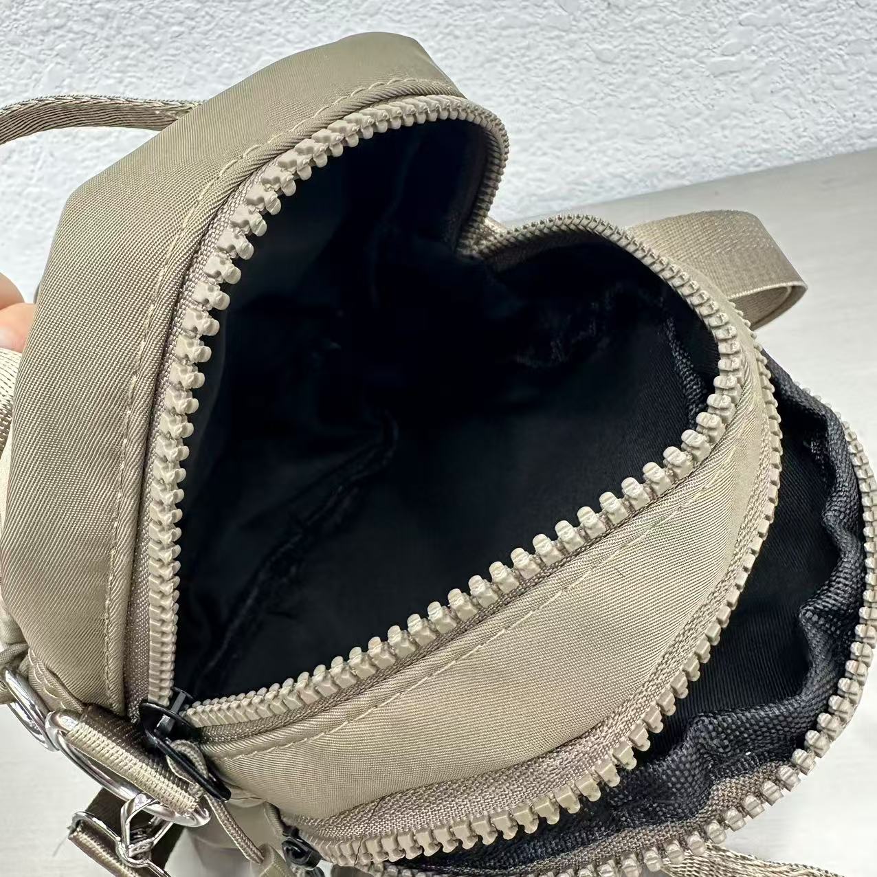 Beige backpack with a zipper open, showing black interior on a textured white background,A high-fashion shot of a woman in a black skirt and white shirt, holding a stylish, minimalist brown bag. The image is professionally lit in a studio against a clean white background, with a strong focus on the bag's sleek design and texture. The photo emphasizes a sophisticated and modern aesthetic, perfect for luxury or premium lifestyle brands.