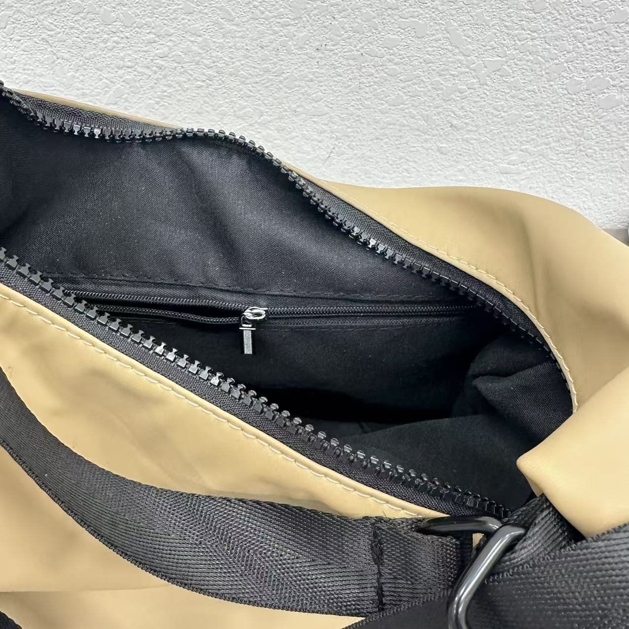 Close-up of a beige and black bag with a zipper on a textured gray background,laptop tote bag for women, tote bag for office use, college tote bag with zipper, and stylish bags for girls. You can also target users with specific needs by using long-tail phrases like vegan leather tote bag or tote bag for daily use in India. To understand the market better, keep an eye on competitors such as Lavie, Baggit, and Caprese, all of which are major players in the Indian handbag space, along with brands like Zouk and