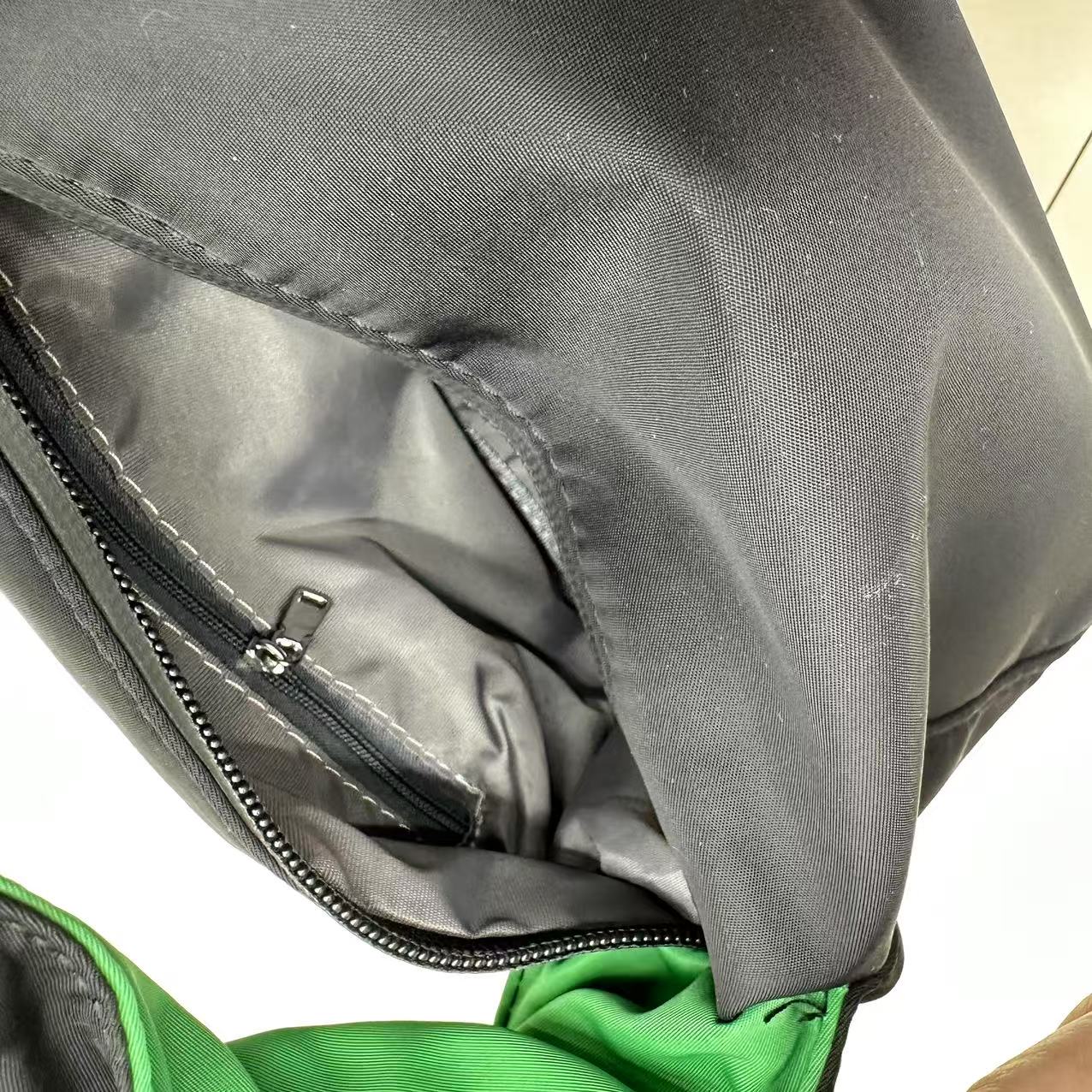 Close-up of a gray backpack with a partially open zipper, showing green fabric inside."Black waterproof polyester mini tote bag with stylish green lining, lightweight and durable design, adjustable crossbody strap and spacious compartments for wallet, phone, cosmetics and daily essentials. Perfect handbag for women in India for office, college, travel, shopping, and everyday use. Premium quality ladies tote bag available online at best price in India, versatile small carry bag for students, professionals, a