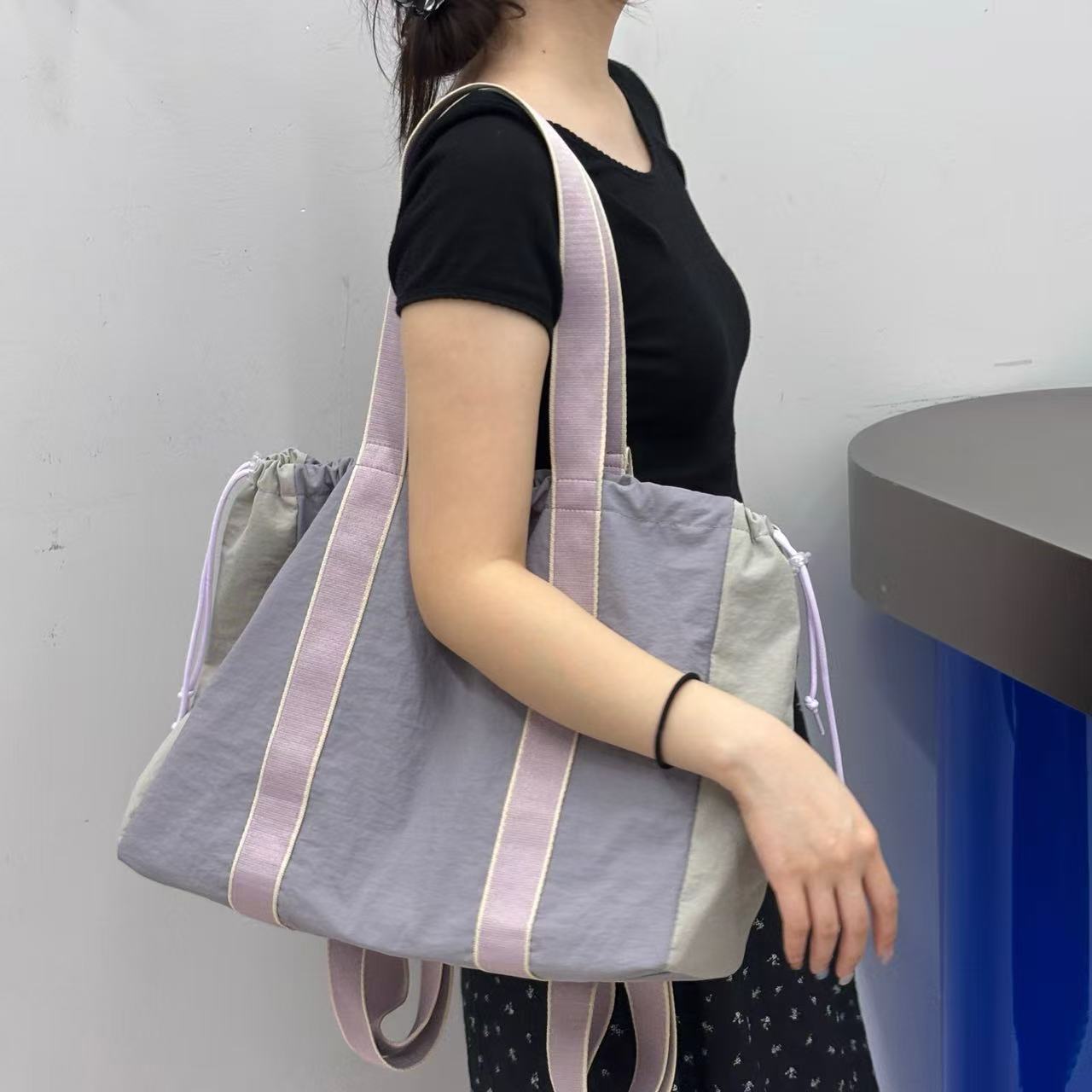 Person holding a gray tote bag with purple straps against a plain background,A versatile and stylish tote bag for women, perfect for the Indian market, shot from a side angle showing the product in use. The bag is made from a durable, high-quality fabric and features a casual, comfortable design with shoulder straps. This fashion accessory is ideal for a daily commute, college, or casual outings. It's a must-have for those seeking a practical yet trendy handbag in India.