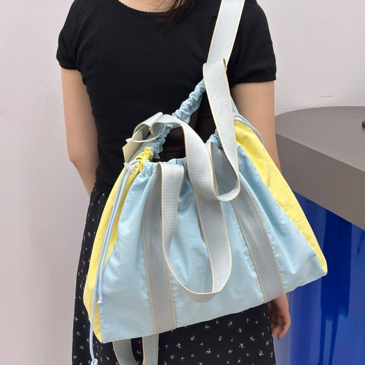 Light blue and yellow bag held by a person against a plain background,v
