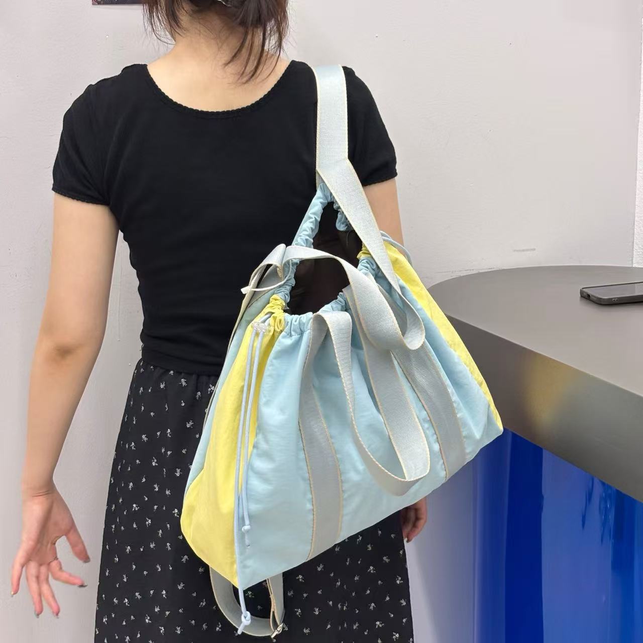 Person holding a light blue and yellow drawstring bag against a plain background,A versatile and stylish tote bag for women, perfect for the Indian market, shot from a side angle showing the product in use. The bag is made from a durable, high-quality fabric and features a casual, comfortable design with shoulder straps. This fashion accessory is ideal for a daily commute, college, or casual outings. It's a must-have for those seeking a practical yet trendy handbag in India.