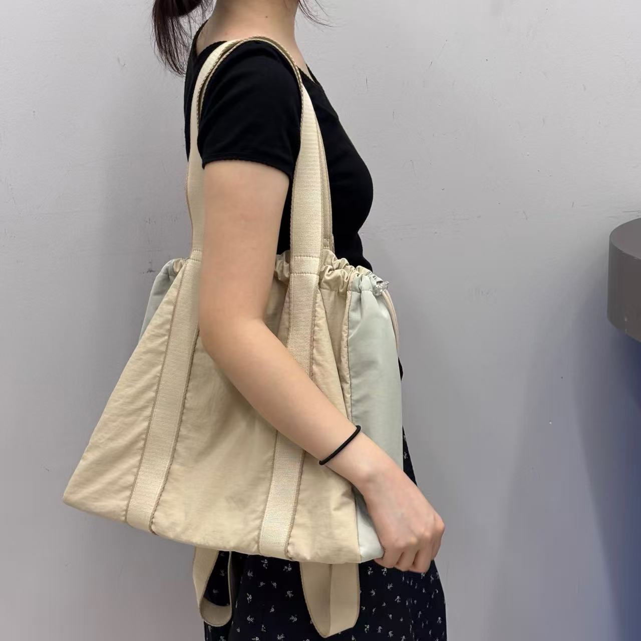 Person holding a beige tote bag against a plain background,A versatile and stylish tote bag for women, perfect for the Indian market, shot from a side angle showing the product in use. The bag is made from a durable, high-quality fabric and features a casual, comfortable design with shoulder straps. This fashion accessory is ideal for a daily commute, college, or casual outings. It's a must-have for those seeking a practical yet trendy handbag in India.