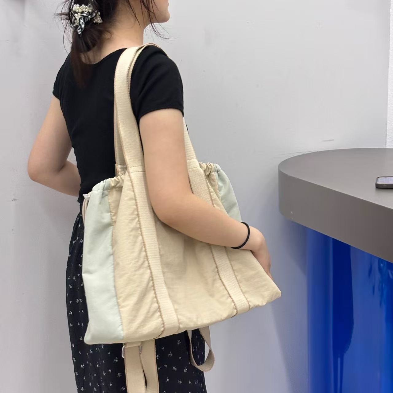 Person holding a beige and white quilted bag against a plain background,A versatile and stylish tote bag for women, perfect for the Indian market, shot from a side angle showing the product in use. The bag is made from a durable, high-quality fabric and features a casual, comfortable design with shoulder straps. This fashion accessory is ideal for a daily commute, college, or casual outings. It's a must-have for those seeking a practical yet trendy handbag in India.