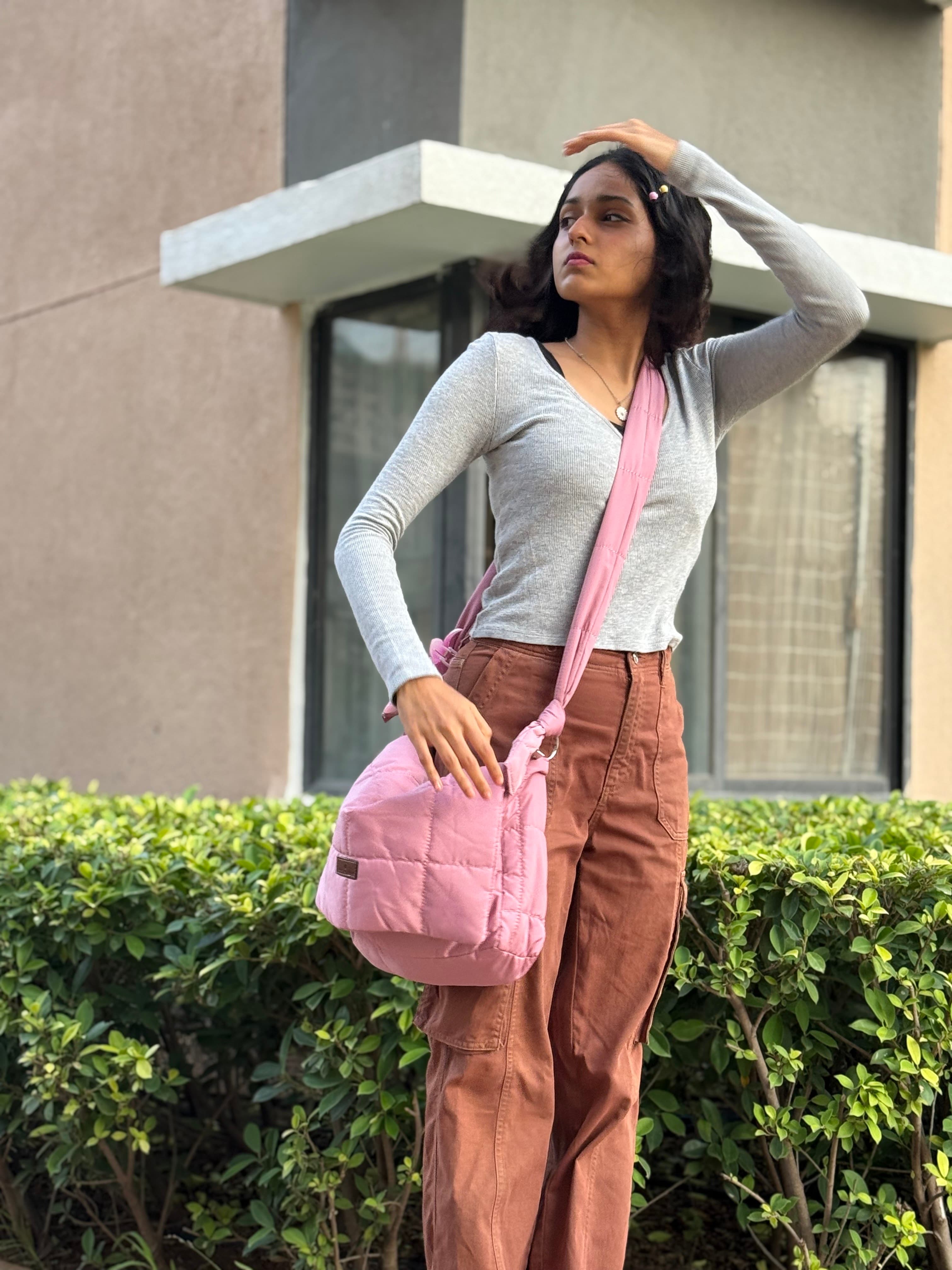 Woman holding a pink bag outdoors with a building in the background Quilted shoulder bag with a padded design, knotted strap detail, and soft structured silhouette – lightweight, functional, and perfect for daily use or casual outings. Compact yet spacious, ideal for carrying essentials in style. A statement accessory from Tales of Totes, offering cozy fashion-forward appeal for Indian shoppers.