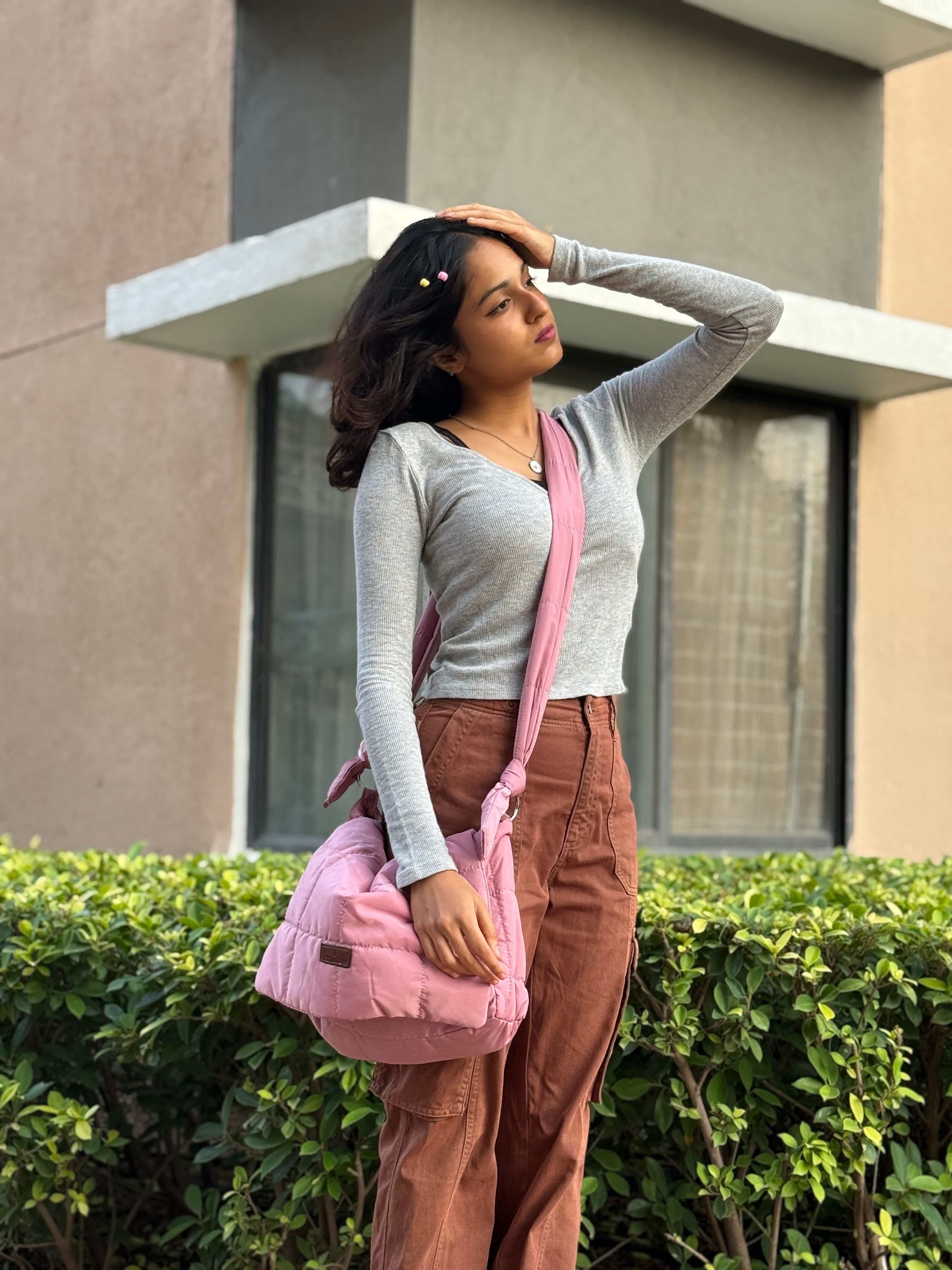 Woman holding a pink bag outdoors with a building and greenery in the background Quilted shoulder bag with a padded design, knotted strap detail, and soft structured silhouette – lightweight, functional, and perfect for daily use or casual outings. Compact yet spacious, ideal for carrying essentials in style. A statement accessory from Tales of Totes, offering cozy fashion-forward appeal for Indian shoppers.
