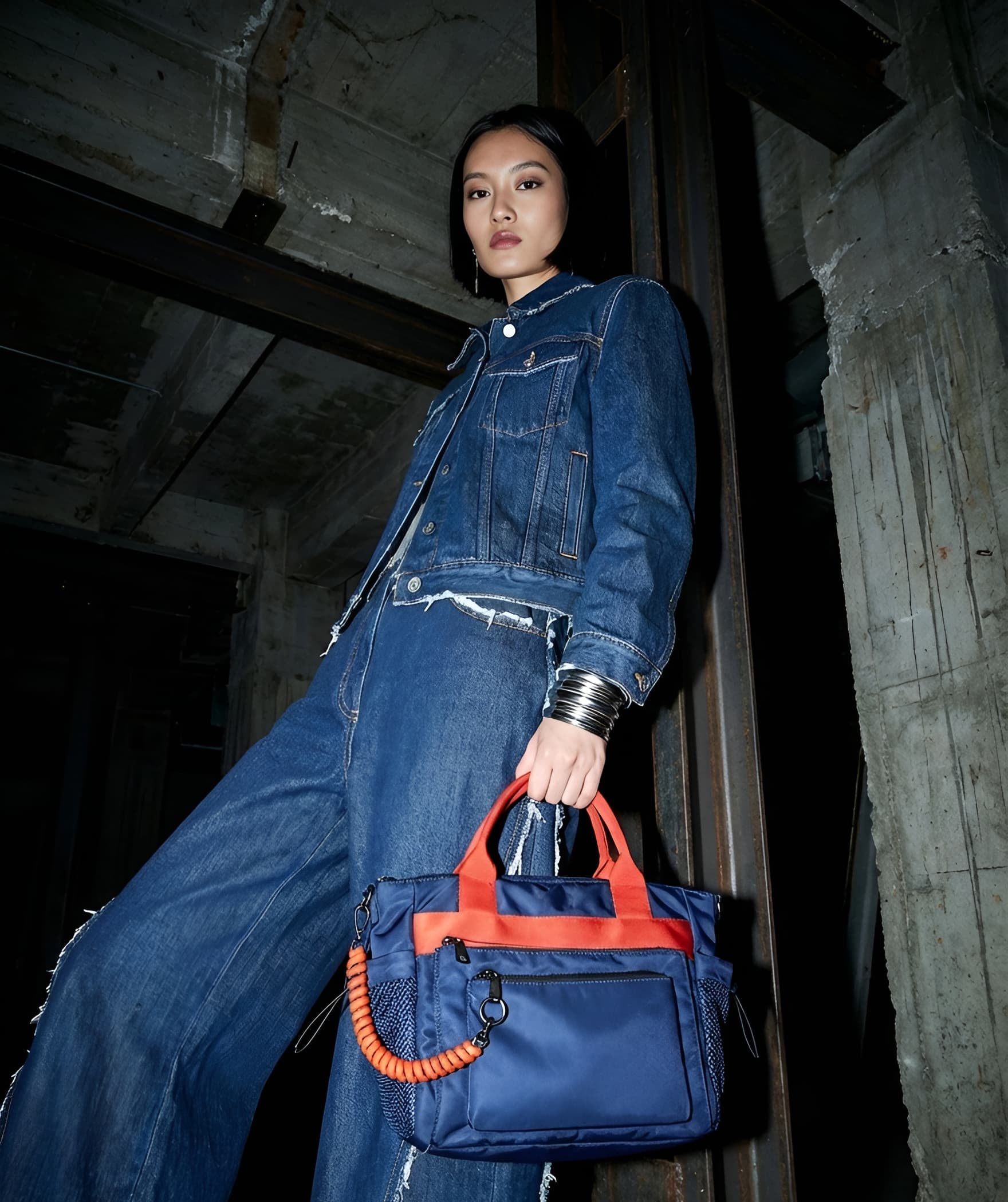 Person wearing a denim outfit holding a blue handbag with orange accents in an industrial setting
