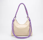 A cream-colored canvas hobo bag with a thick, braided purple shoulder strap featuring multicolor threads, photographed on a white background.