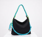A black slouchy shoulder bag with a thick braided blue and yellow rope handle, displayed on a white pedestal against a white background.
