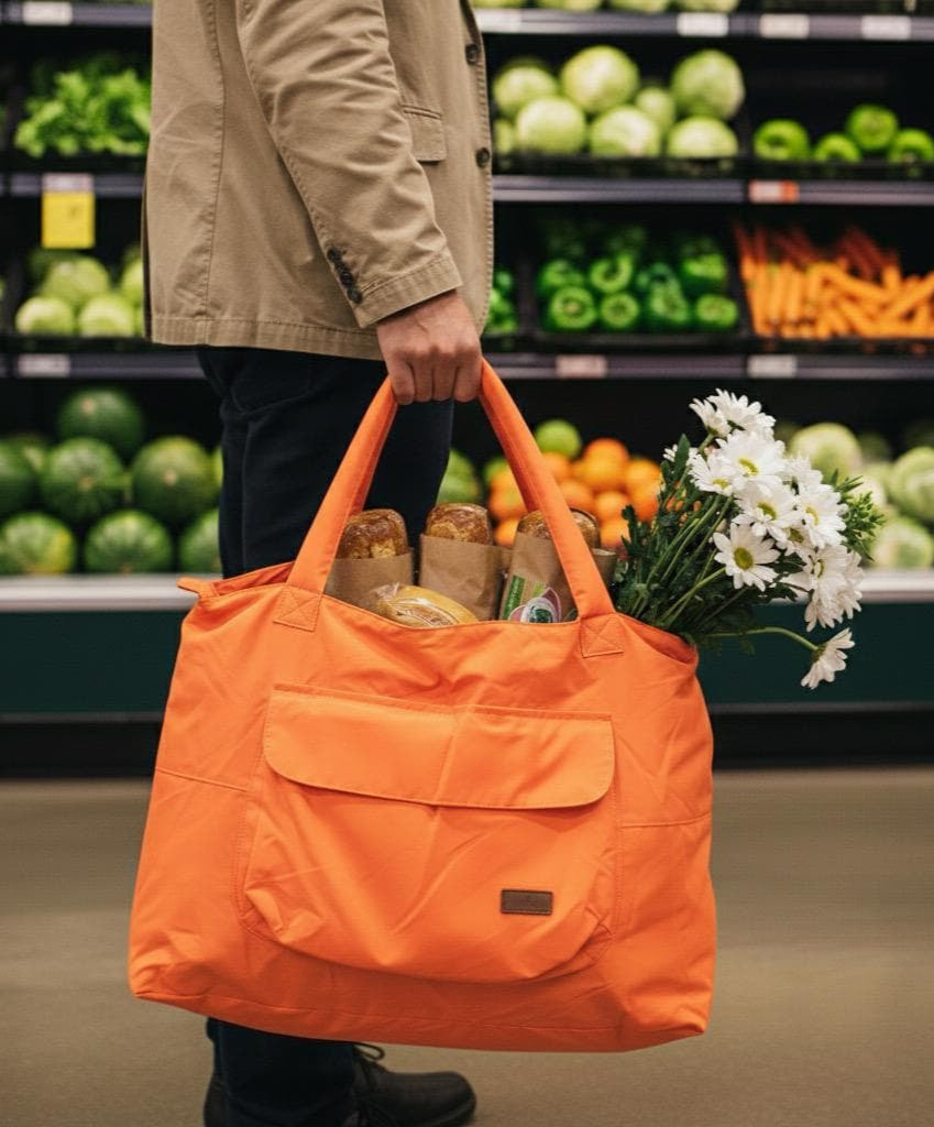 Person holding an orange reusable shopping bag filled with groceries in a supermarket.Person wearing a black coat and holding an orange bag on a white background,Gray tote bag with a hand reaching in to place a bottle, on a white backgroundLightweight nylon tote bag with a padded handle design and front flap pocket – perfect for everyday errands, gym, shopping, or casual travel. Spacious, foldable, and easy to carry with a functional structure that balances fashion and utility. A bold statement piece from T