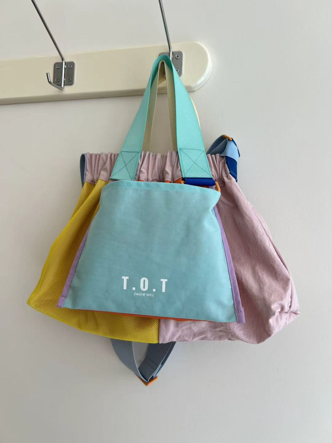 A pastel patchwork tote bag with the text 'T.OT.Trendy multi-color casual college tote bag with mesh detailing and adjustable straps.