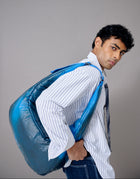 Man carrying a large blue bag over his shoulder against a plain background