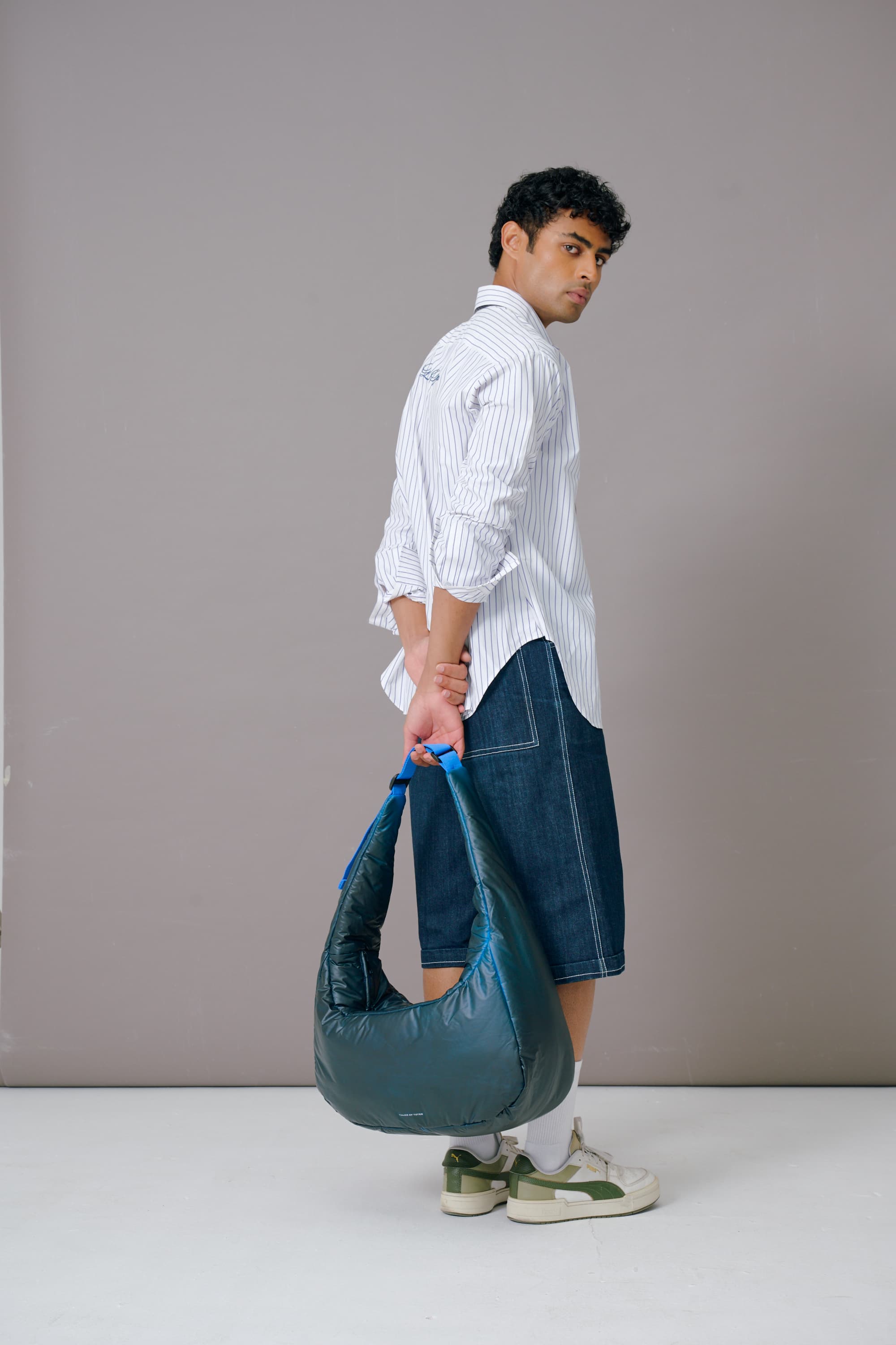 Man holding a blue handbag against a plain background