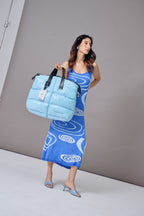 Woman holding a blue textured bag against a gray background