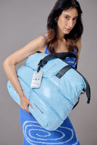 Woman holding a light blue inflatable bag with a visible brand tag against a gray background