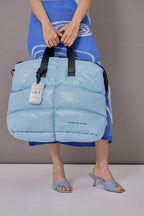 Light blue puffer bag with black straps held by a person wearing a blue outfit.
