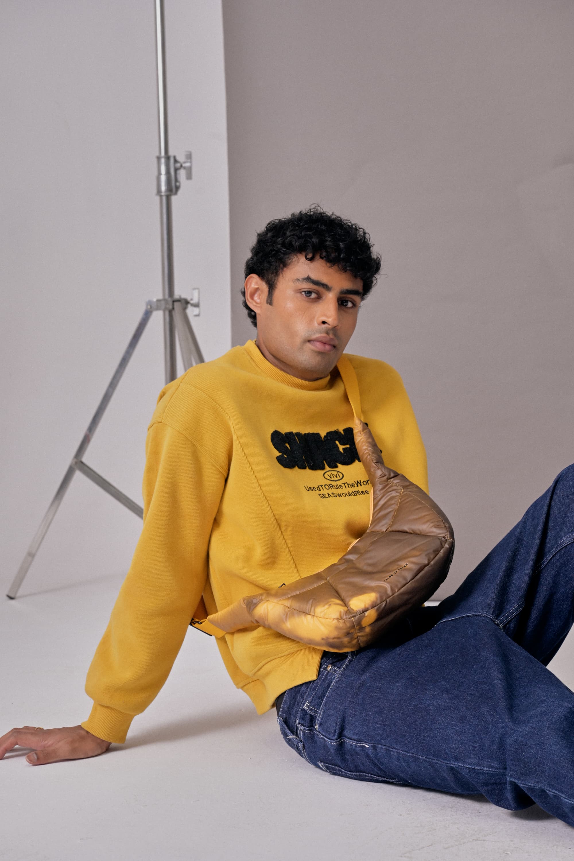 Person wearing a yellow sweatshirt with text and blue jeans sitting on the floor.