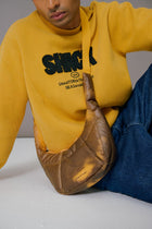 Person wearing a yellow sweatshirt with text, holding a brown leather bag on a light gray background