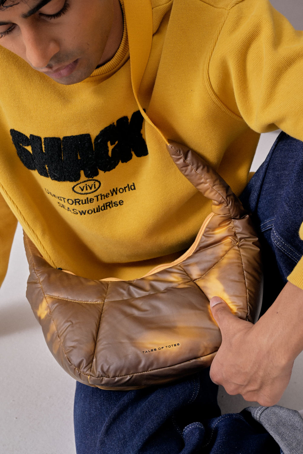 Person wearing a yellow hoodie with text, holding a brown puffer bag.