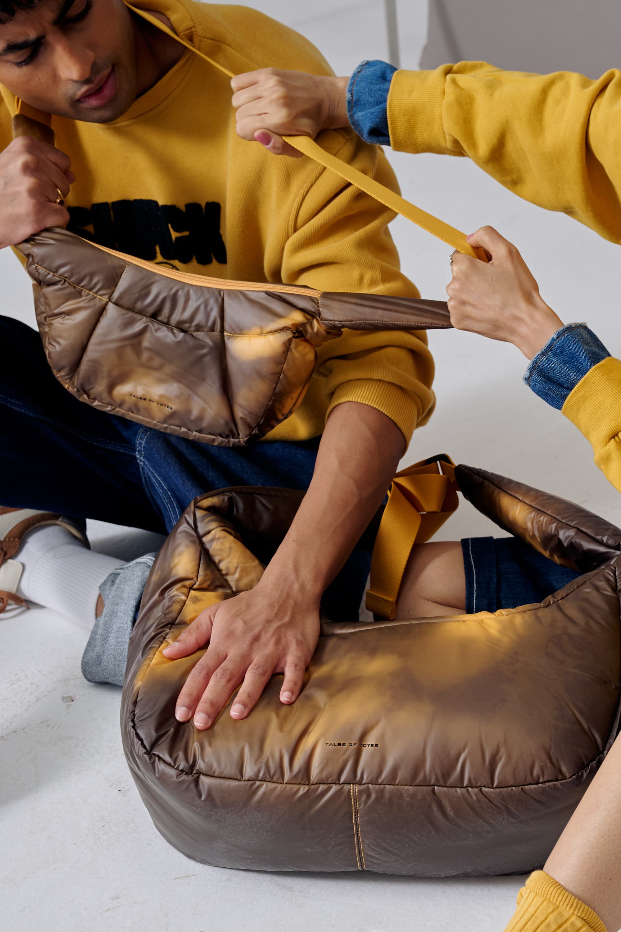 Two people interacting with a large brown leather bag on a light gray floor.
