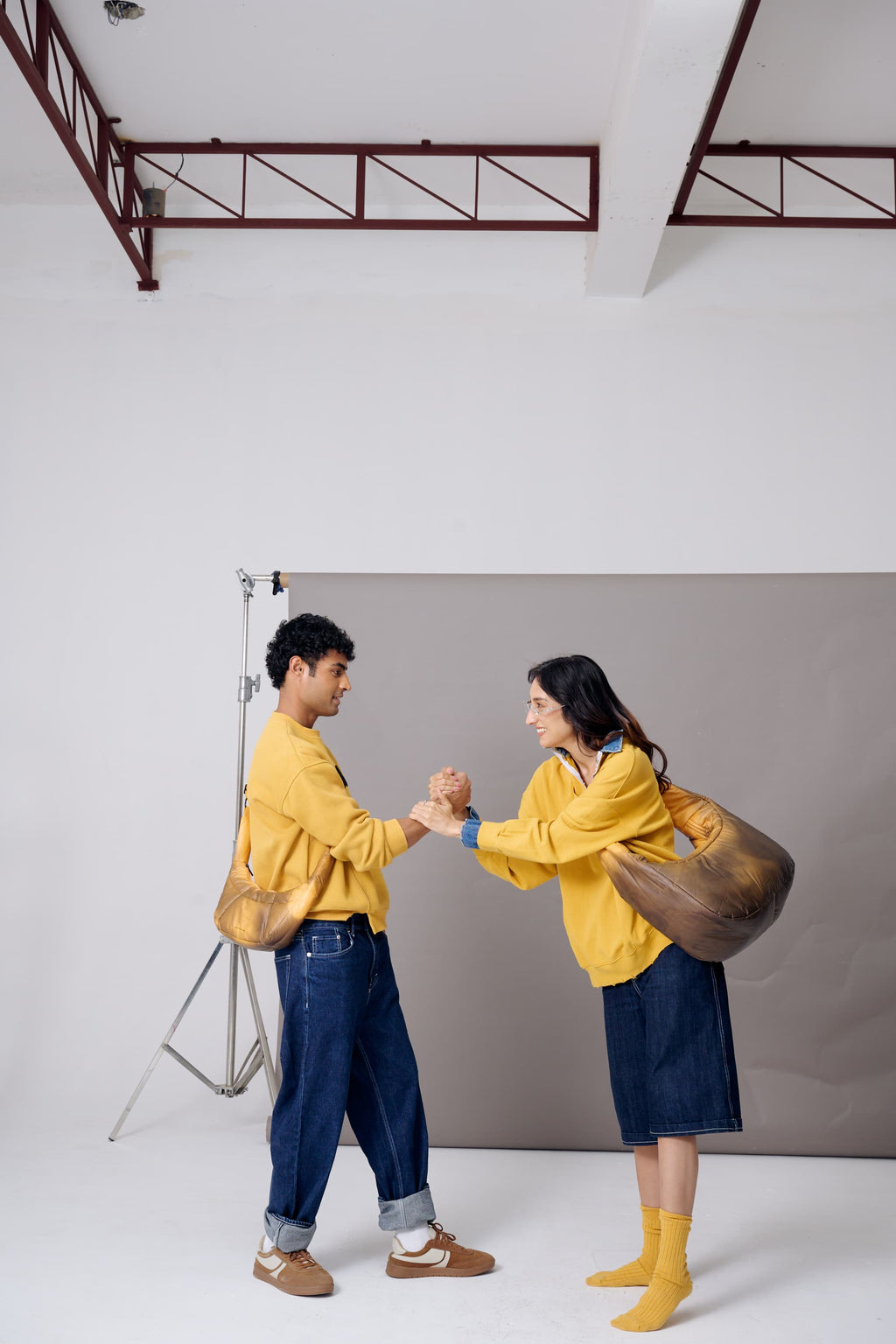 Two people in yellow jackets standing in a studio setting with a gray backdrop.