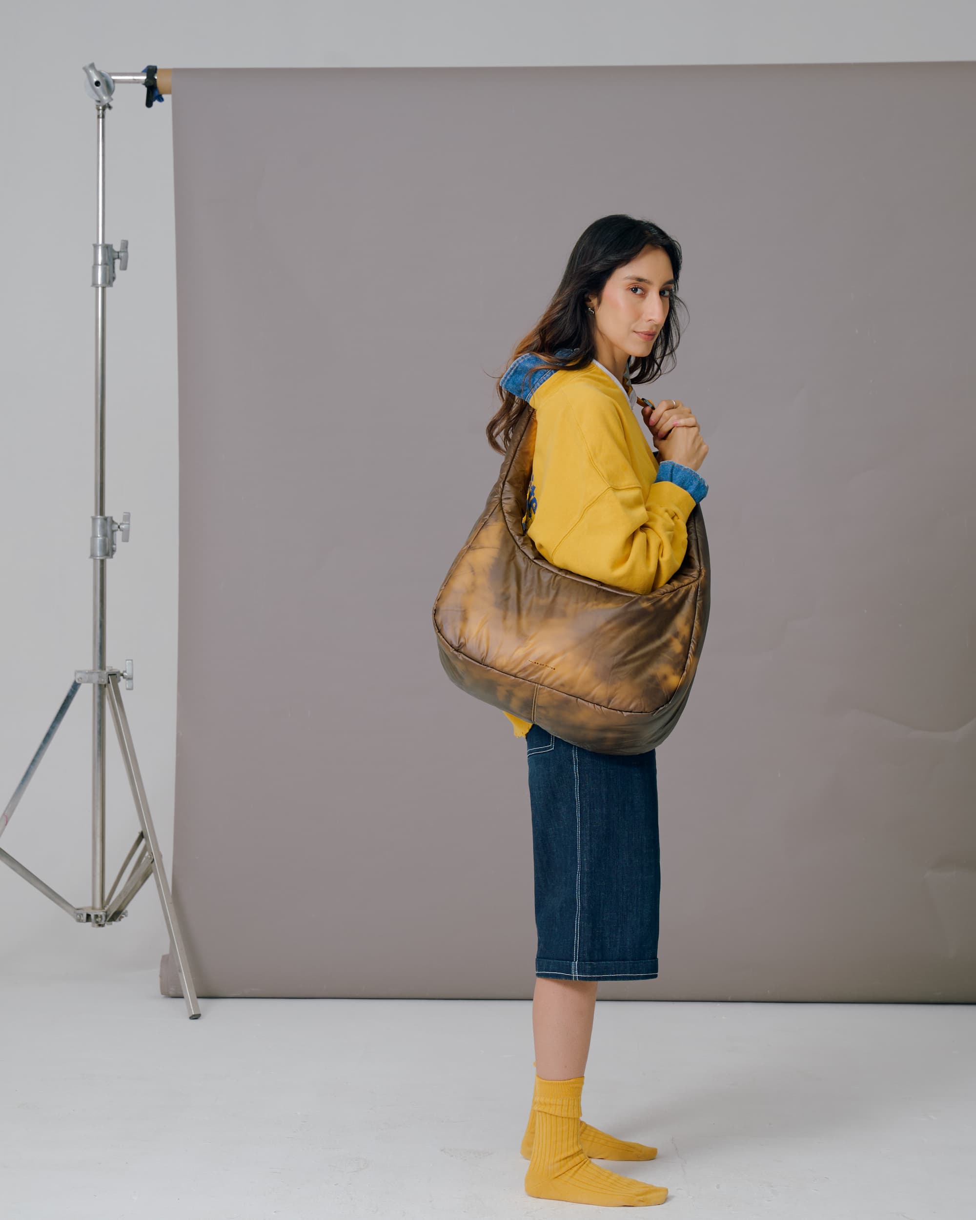 Woman holding a large brown bag against a gray backdrop