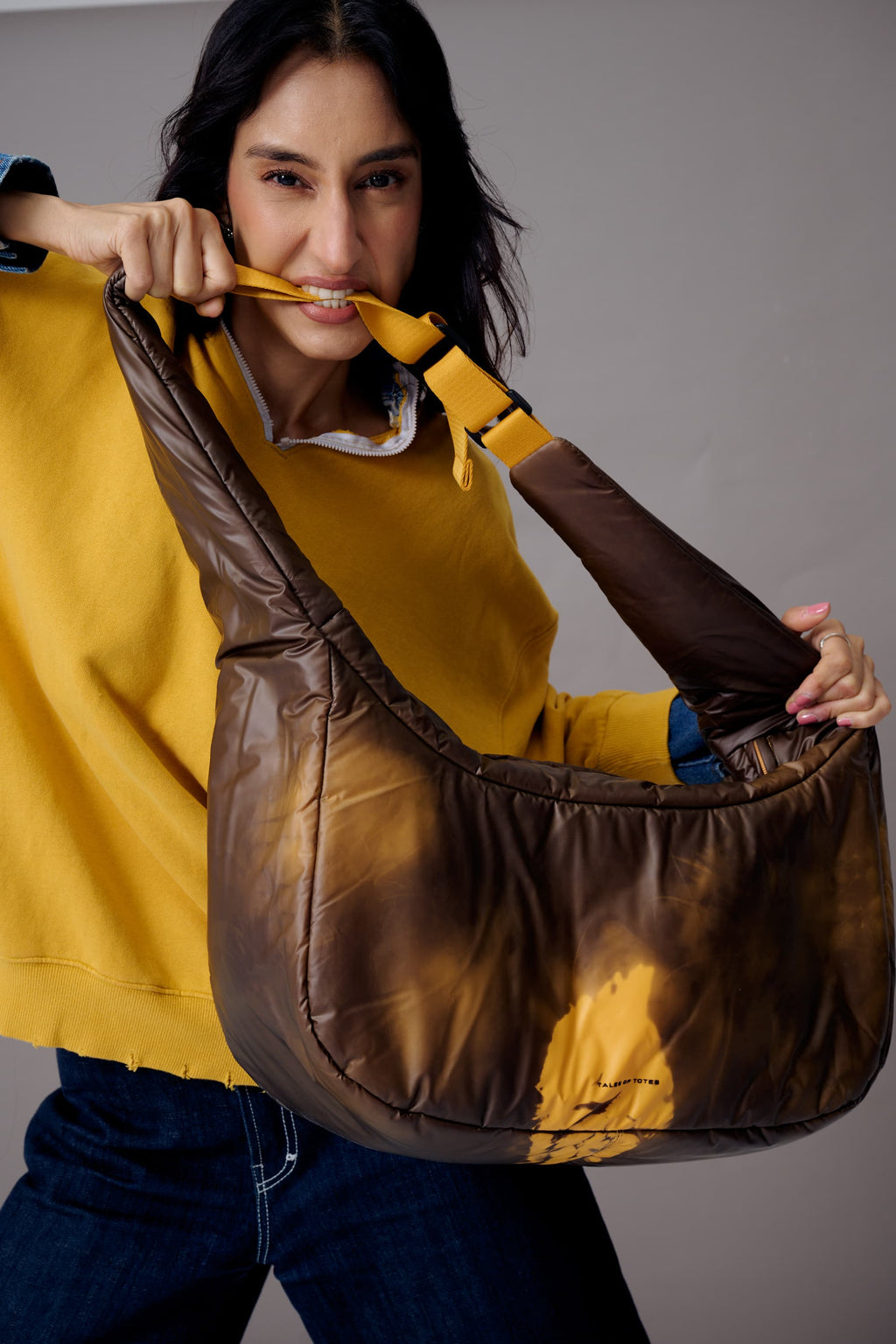Woman holding a large brown leather bag against a gray background