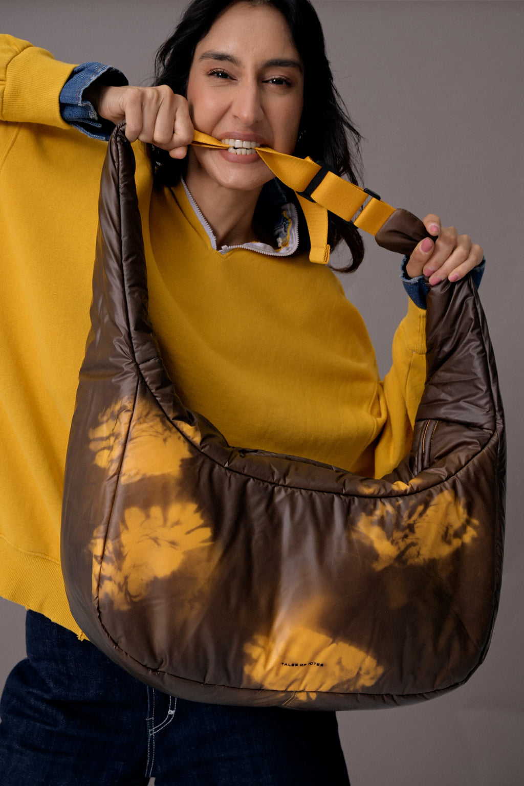 Woman holding a large brown bag with a yellow pattern against a gray background