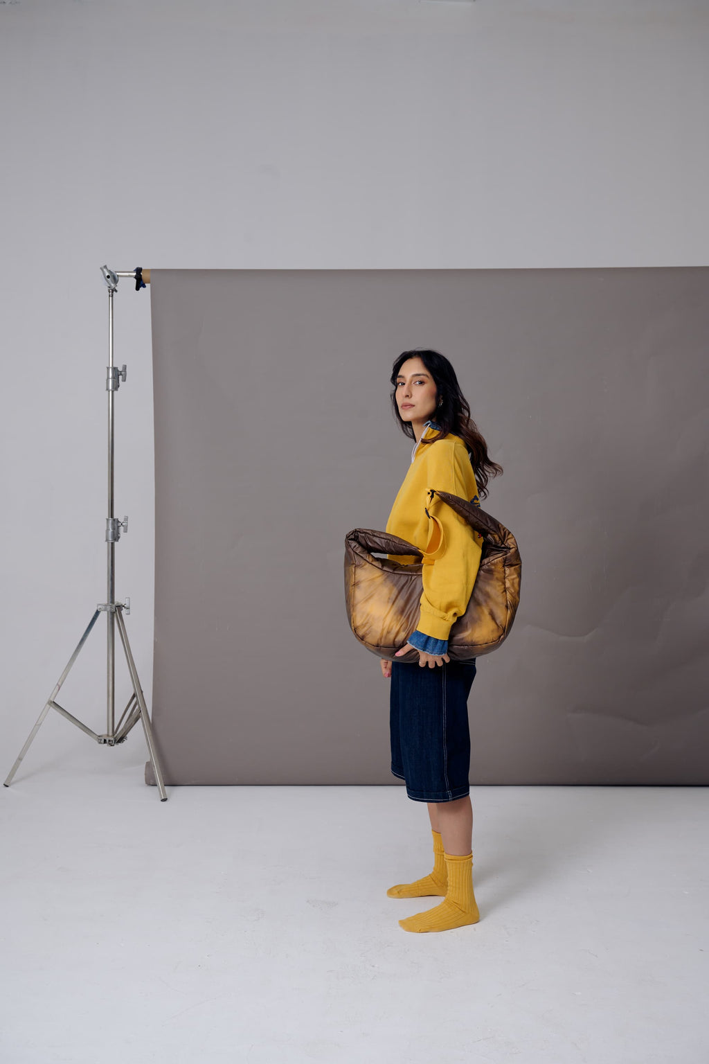 Woman holding a large woven basket in a studio setting with gray backdrop and white floor.