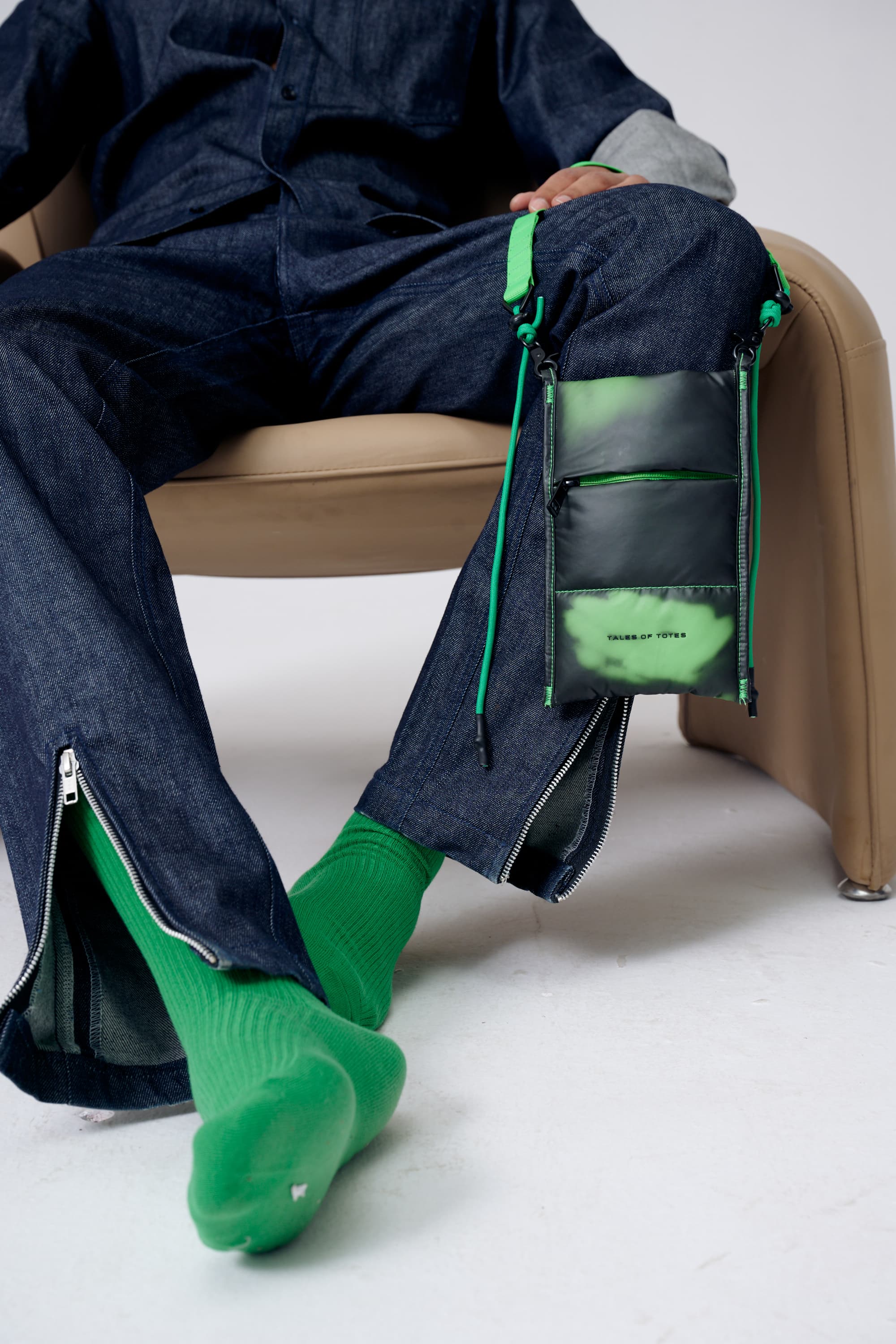 Person wearing a dark outfit with green accents sitting on a chair.