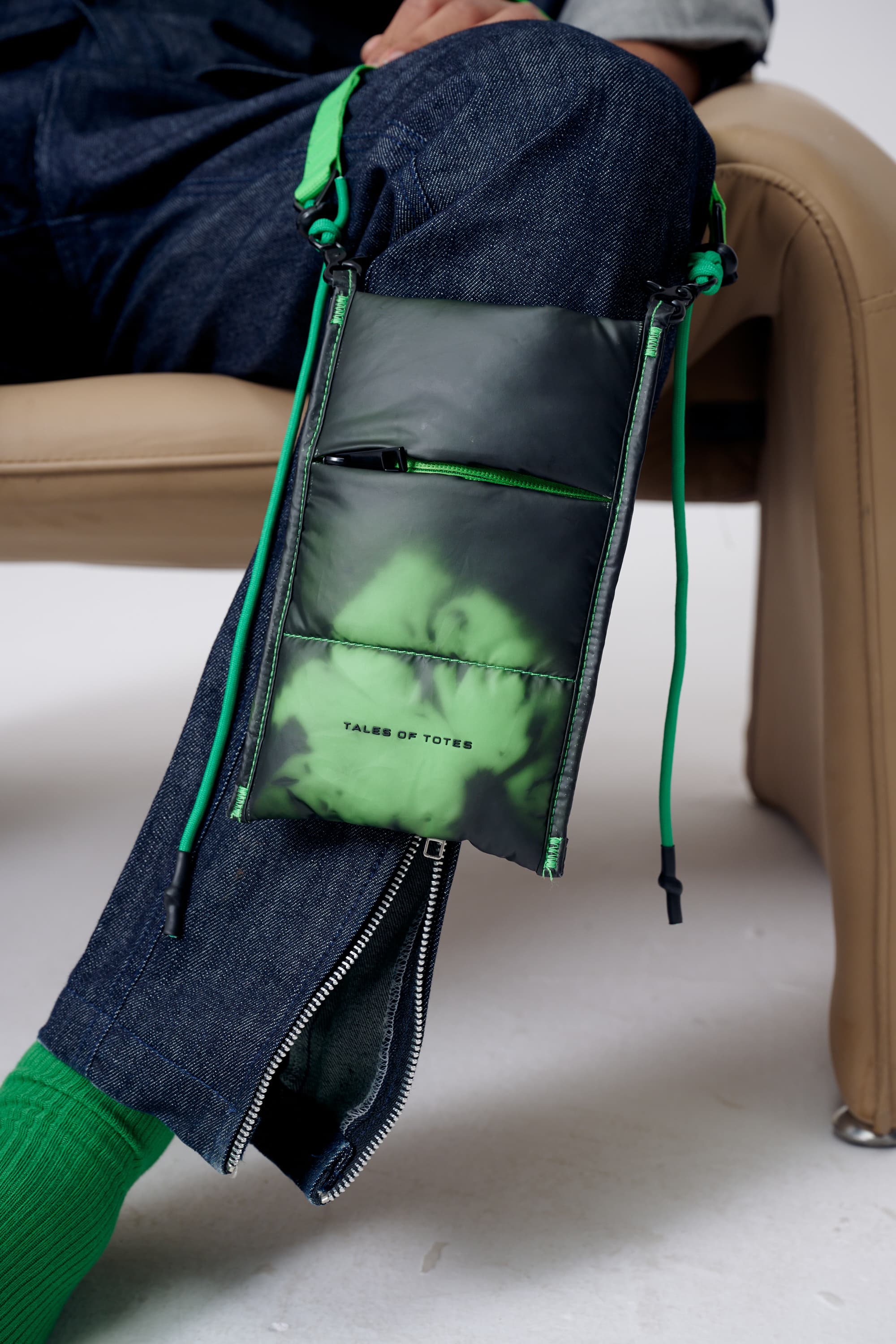 Person sitting on a couch with a black bag featuring green graphics and text.